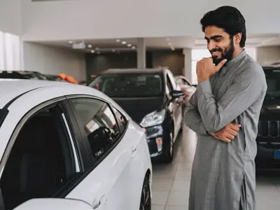 A man considering which car to buy while standing in a dealership showroom