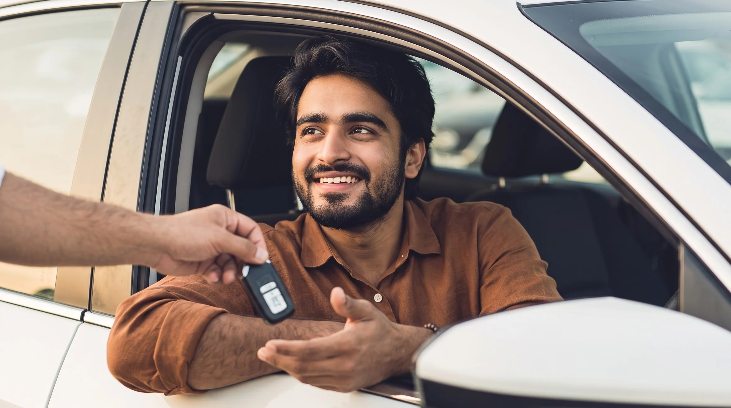 Smiling buyer sitting in the driver's seat of a car, receiving the keys from the seller