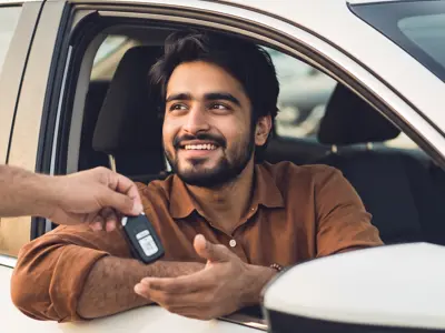 Smiling buyer sitting in the driver's seat of a car, receiving the keys from the seller